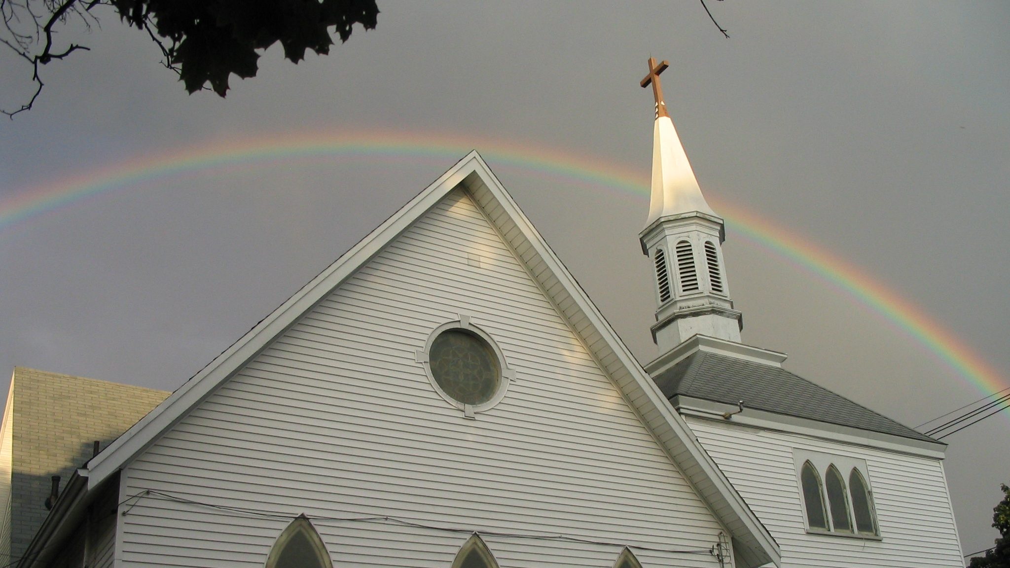 A picture of the First Lutheran Church building, a white New England congregation with a steeple, under a rainbow